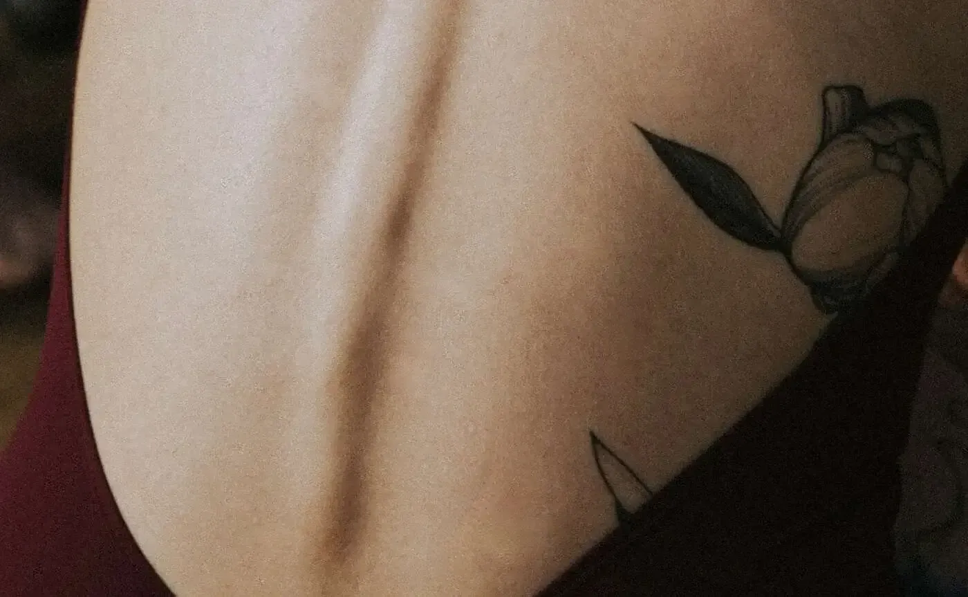 Close-up of a person's bare back, showing the spine and two floral tattoos on the rib area.
