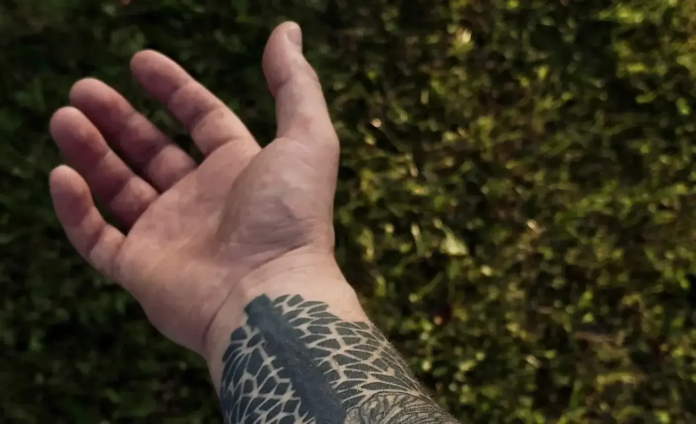 Hand with tattoo on wrist against a blurred mossy background seeking tattoo removal in Vancouver, BC