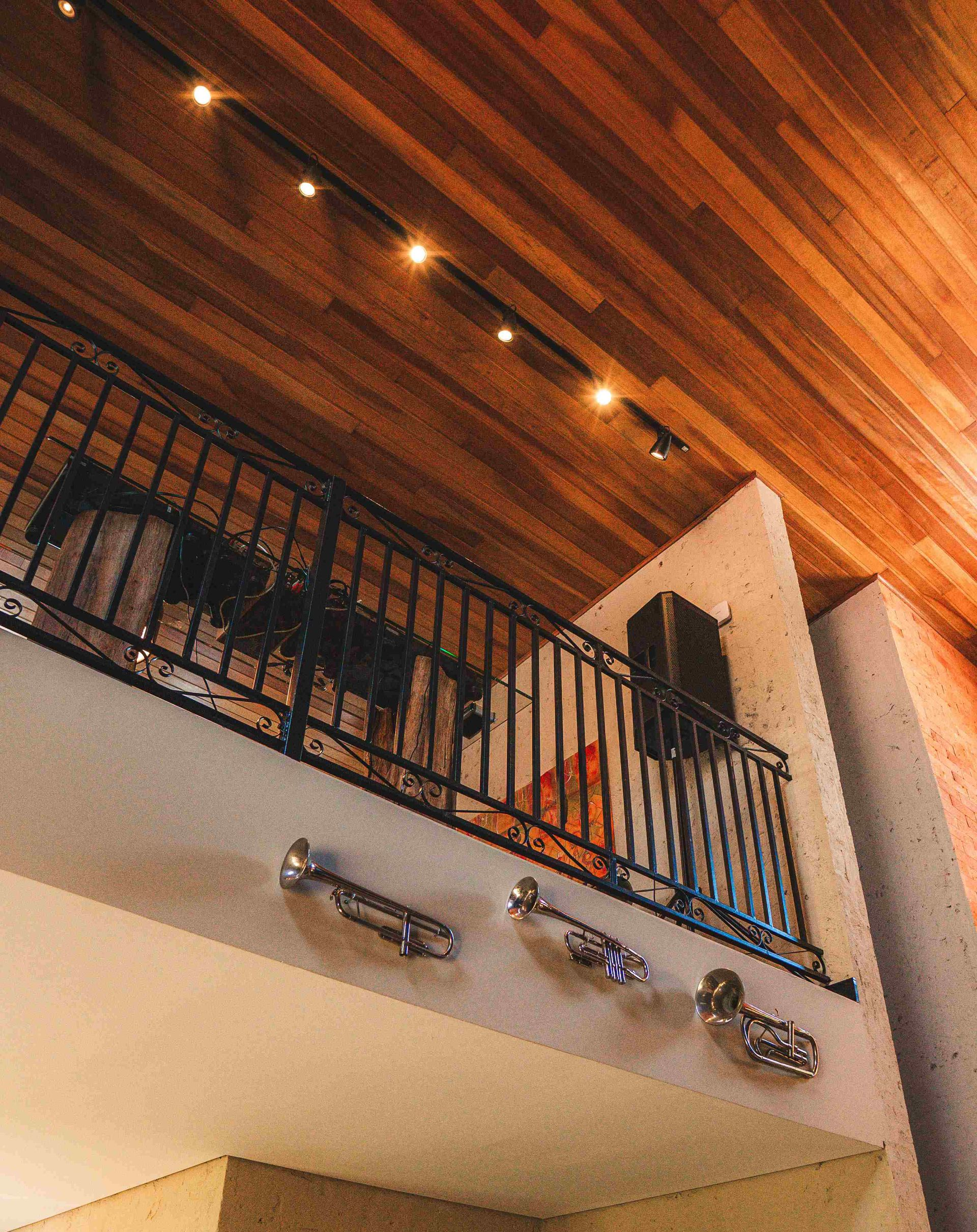 Um loft com teto de madeira e corrimão de metal preto, decorado com trompetes fixados na parede abaixo.