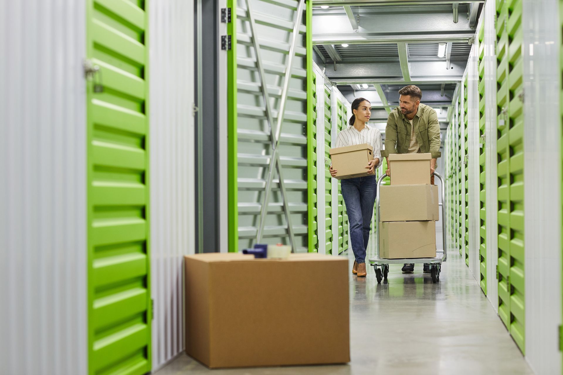 couple holding cardboard boxes walking towards storage unit.