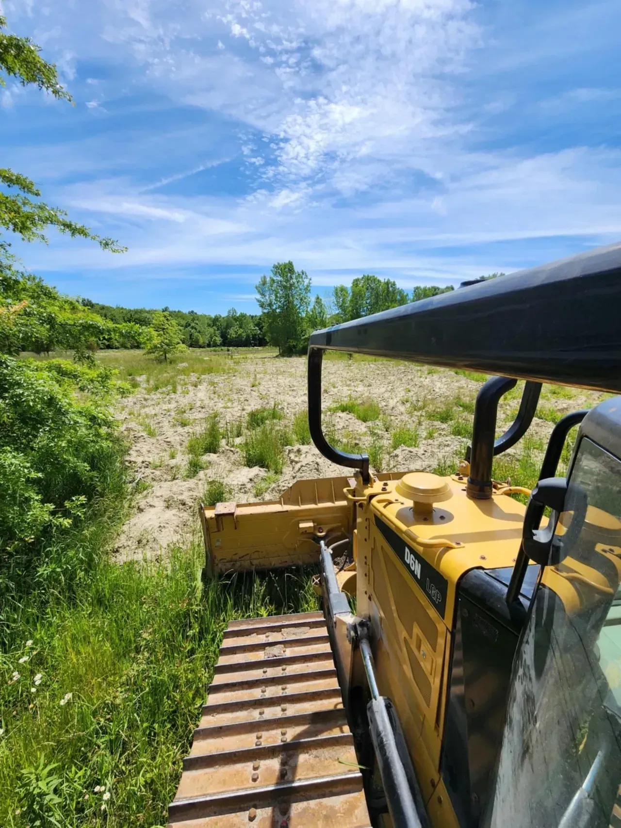 Yellow bulldozer clearing brush on a sunny day with blue sky.