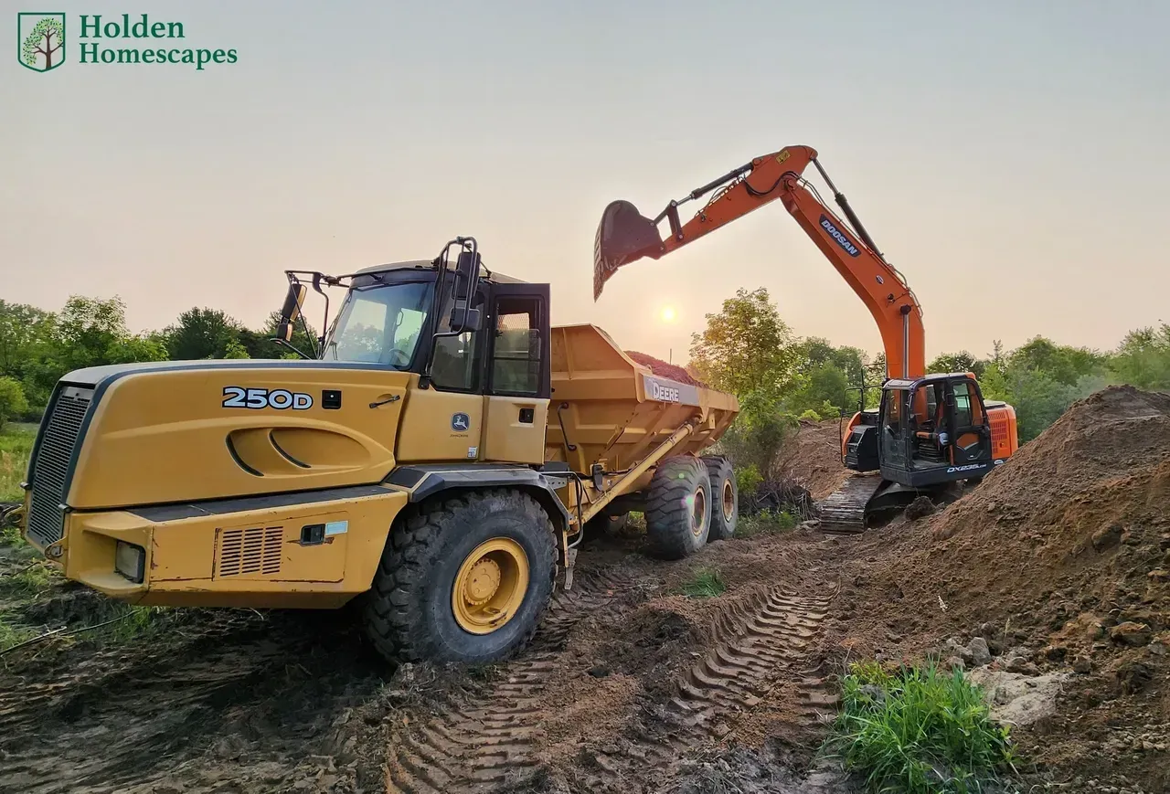 Yellow dump truck and excavator working in a field at sunset, moving dirt.