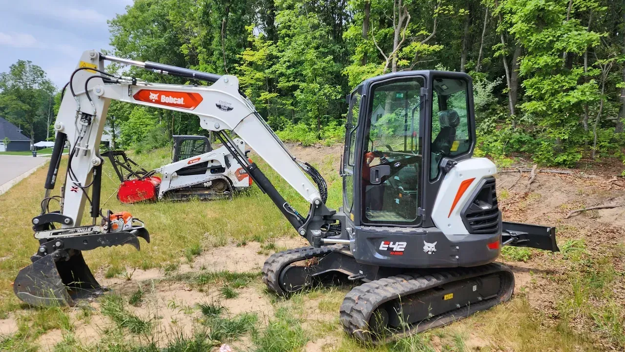 Bobcat excavator on grass with a wooded backdrop.