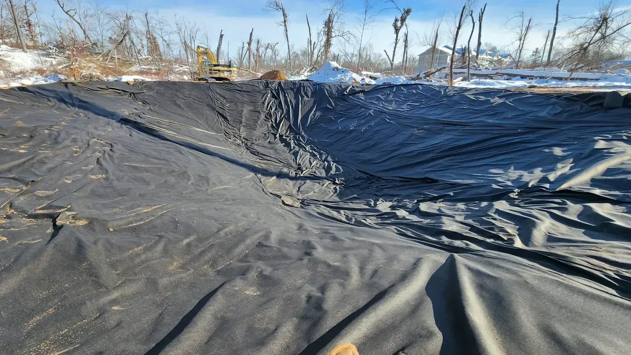 Large, black liner in a dug-out area, possibly for a pond, with tracks from machinery. Winter setting.