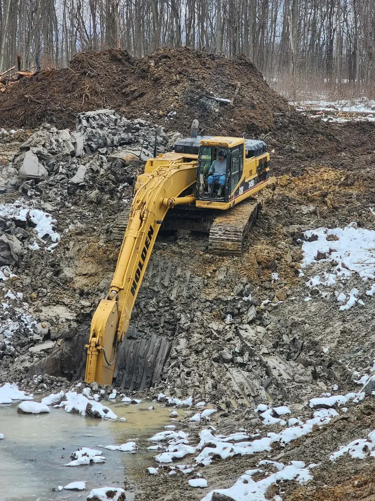 Yellow excavator digging in muddy terrain.