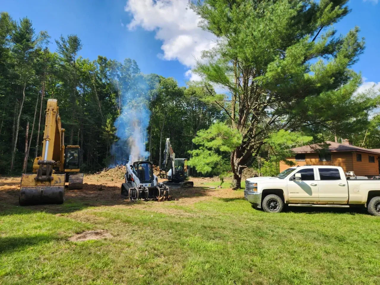 Construction site with excavators, a skid steer, burning debris, and a pickup truck.