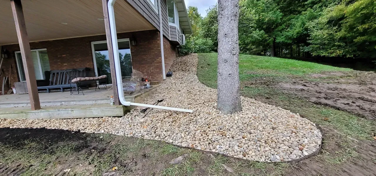 A house with a stone border around a tree. Grass and trees in the background.