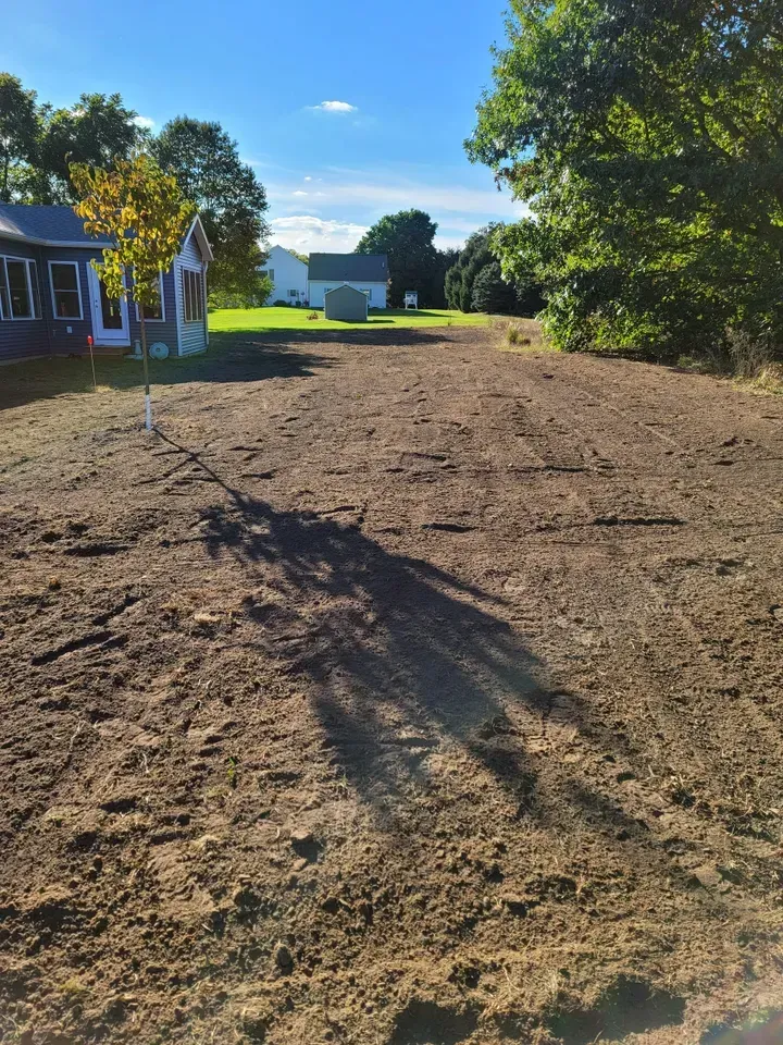 Prepared soil in a yard, trees and houses in the background on a sunny day.