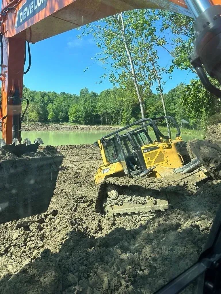 Yellow bulldozer stuck in mud near a pond, being assisted by an orange excavator.