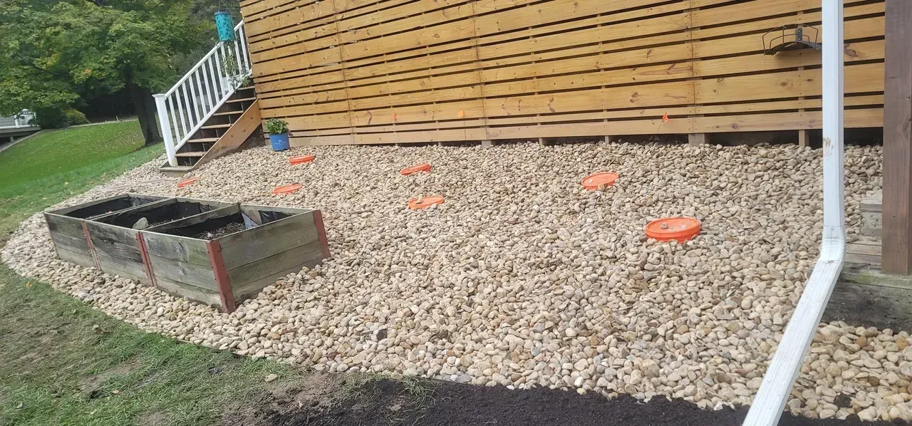 A wood-sided building with a gravel bed, a white railing, and a raised garden bed.