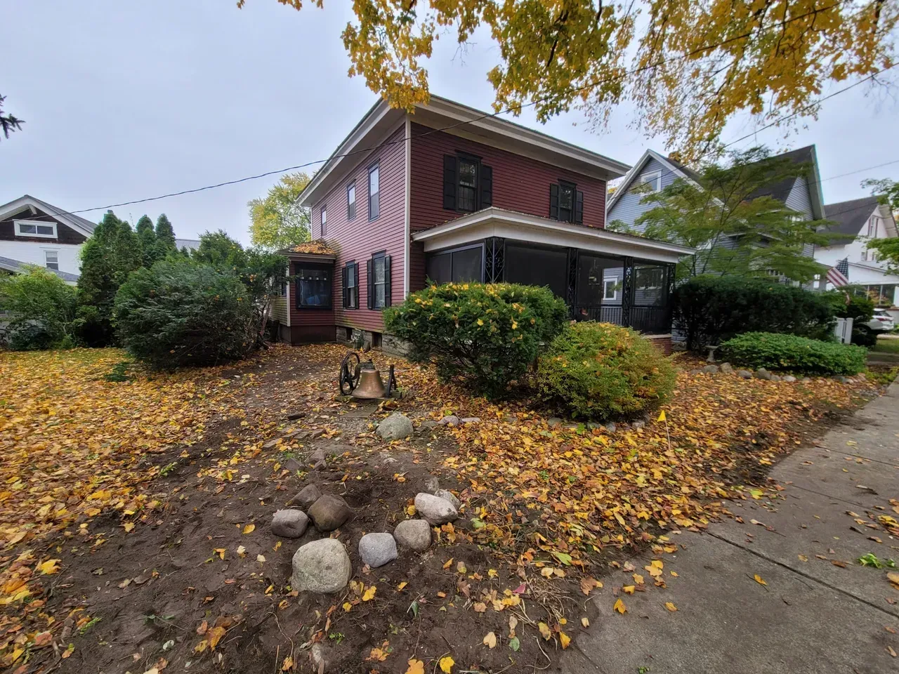 Two-story red house with a porch and yard covered in fallen yellow leaves.