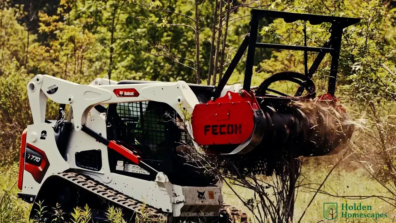 White skid steer with a red brush cutter mulching vegetation in a wooded area.