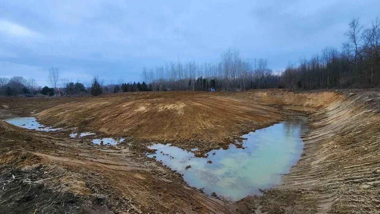 Newly dug earthen pond with muddy water and a cloudy sky.