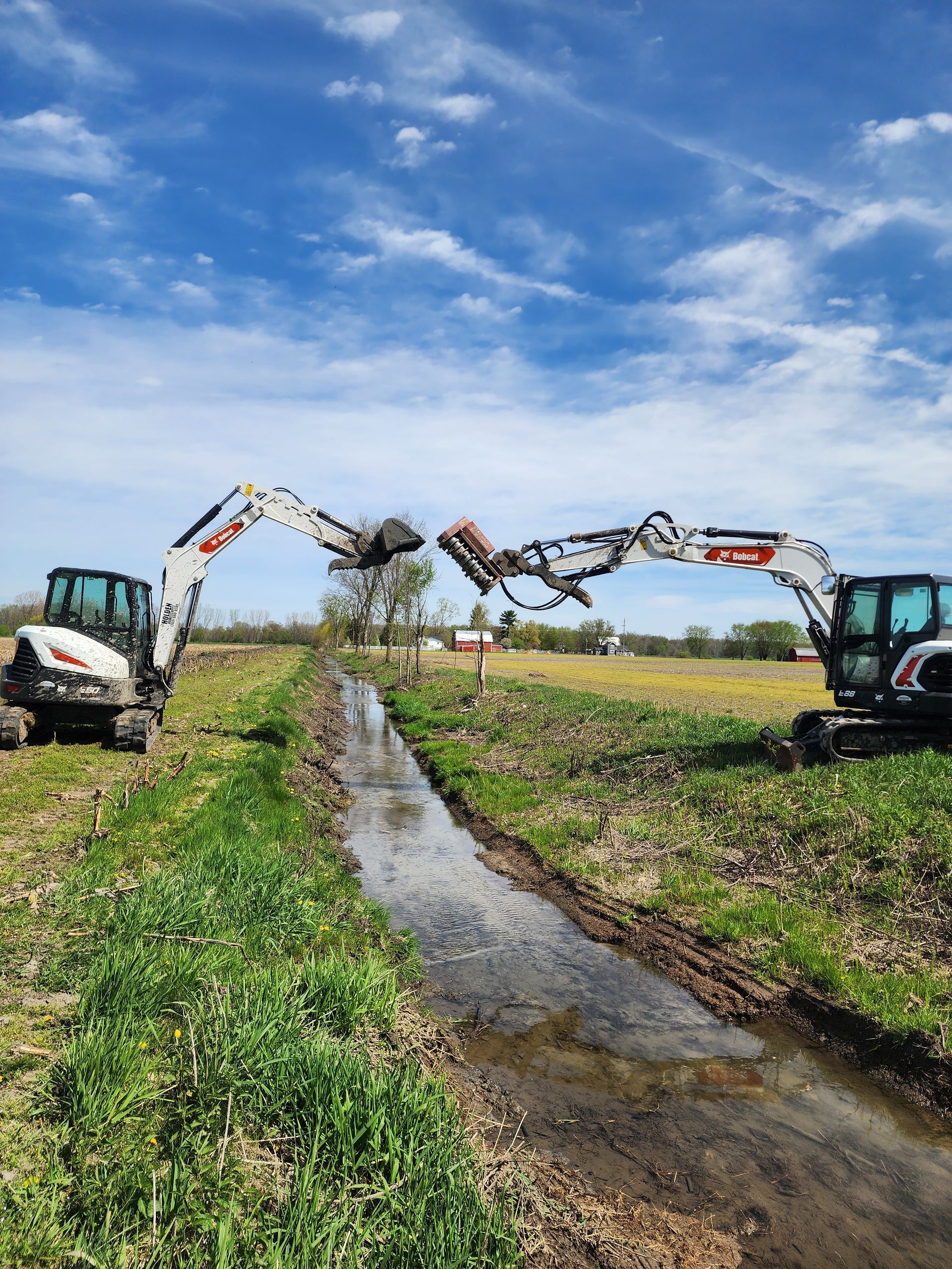 Two white excavators clearing a ditch, under a blue sky.