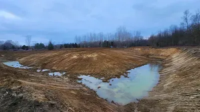 Muddy construction site with water pooling, trees in the background, overcast sky.