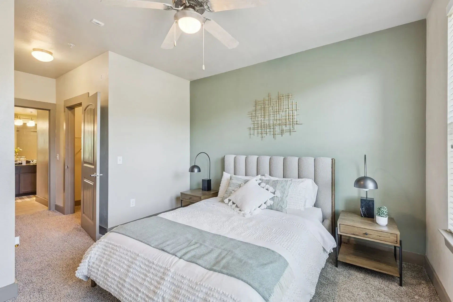 Bedroom with bed, green wall, mirror, art, lamp, and doorway to bathroom.