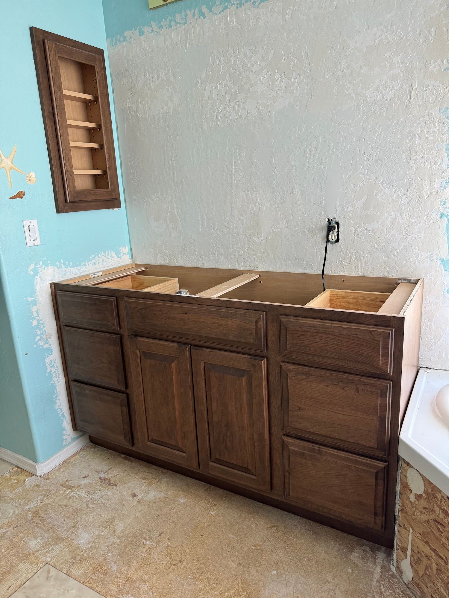 Wooden bathroom vanity with drawers and cabinets installed against a textured blue wall.