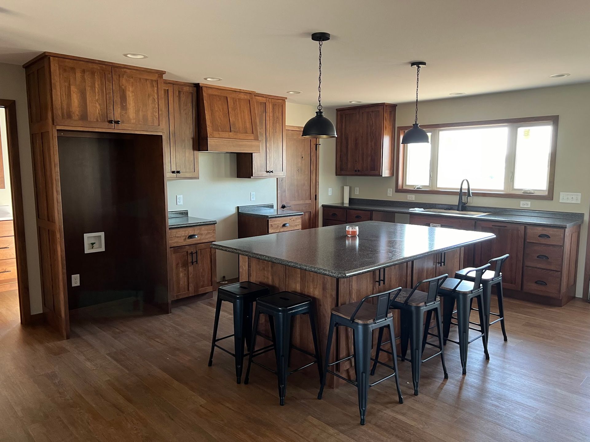 A kitchen with wood cabinets, dark countertops, a central island with stools, and pendant lights.
