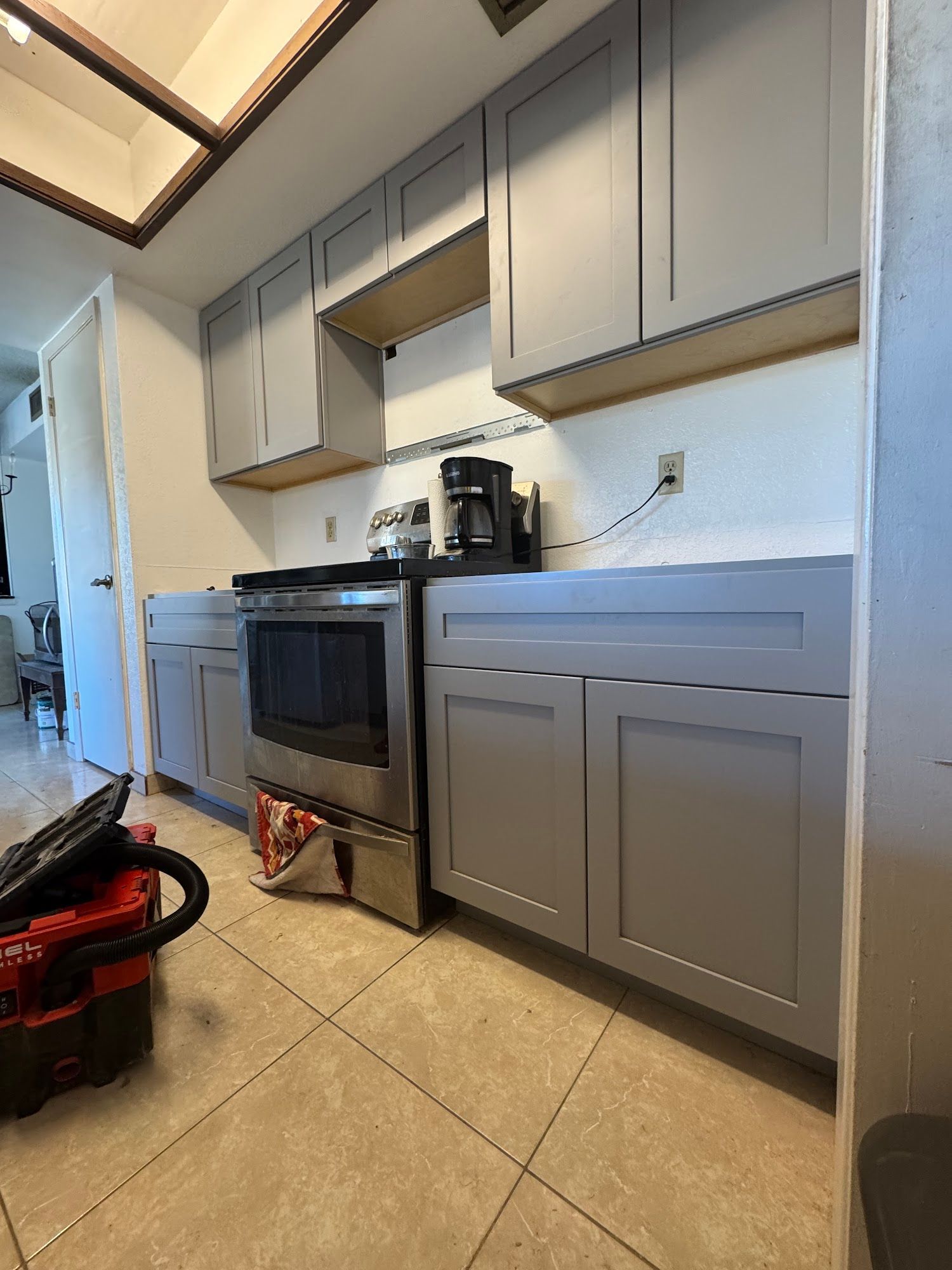 Gray kitchen cabinets installed above and below, a stainless steel oven and coffee maker.