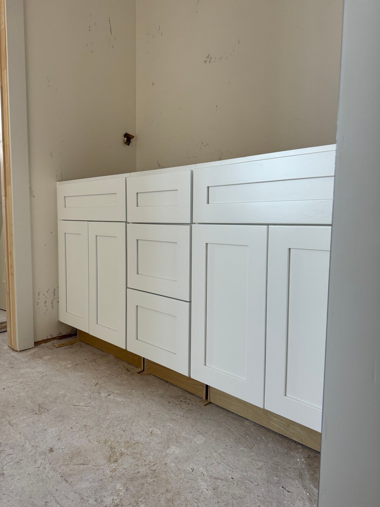 White bathroom vanity with shaker-style doors and drawers against a light-colored wall, unfinished construction.