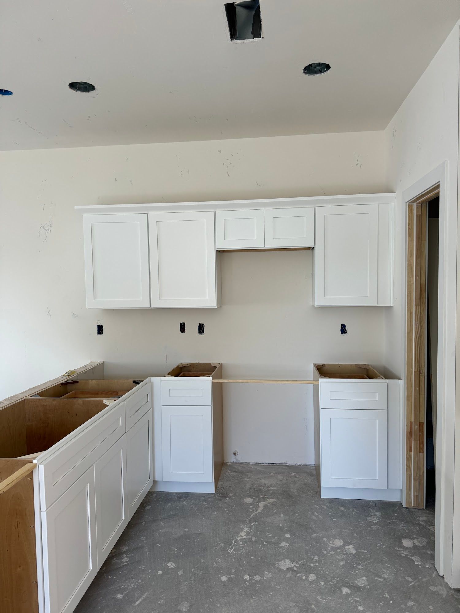 Kitchen under construction with white cabinets and unfinished countertops.