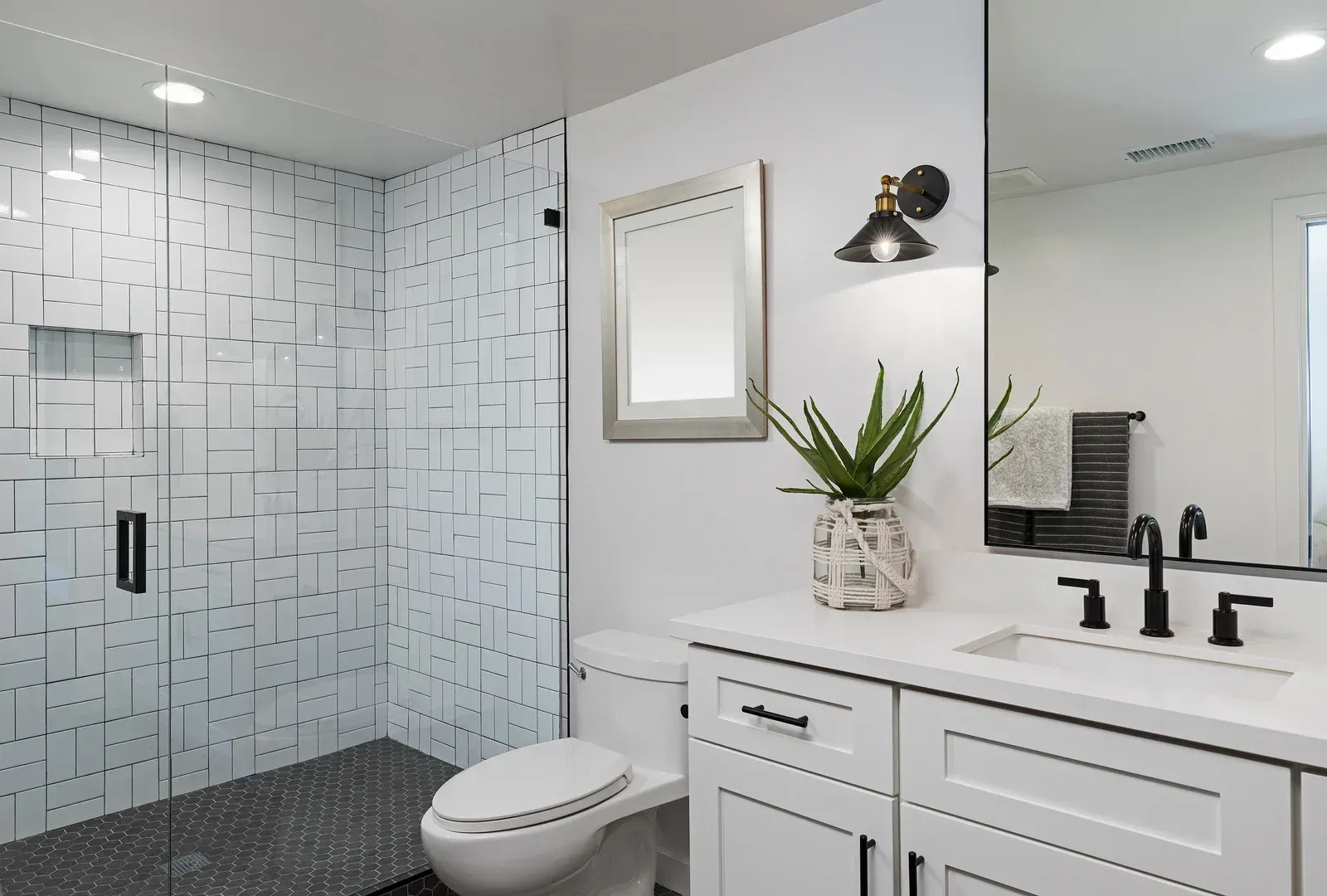 Modern bathroom with white cabinets, patterned shower, and black fixtures.