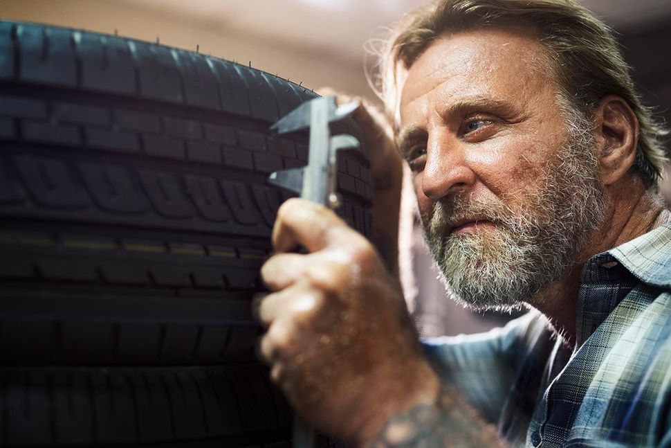 A person with a beard uses a caliper to measure the tread depth of a car tire.