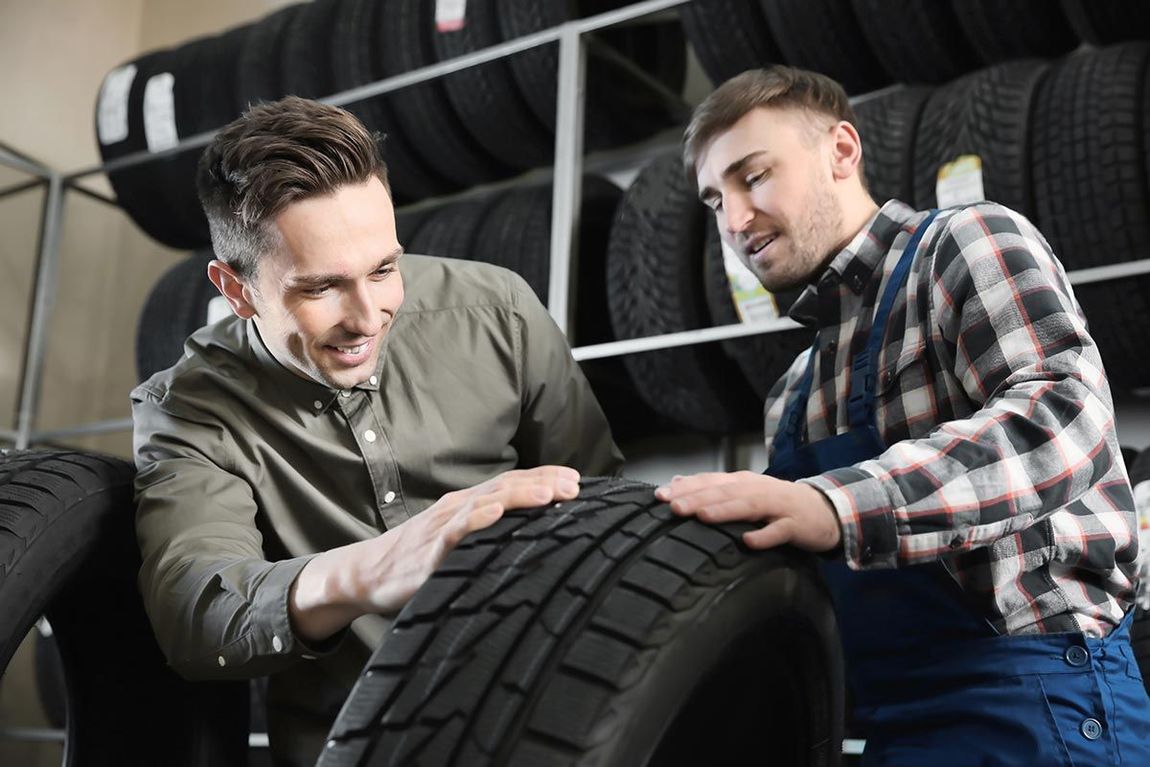 A customer and a mechanic in a tire shop examine a car tire together.
