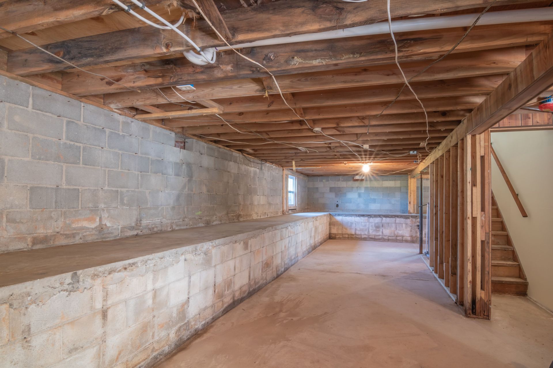 Unfinished basement with concrete block walls, exposed wooden ceiling joists, and a long open walkway