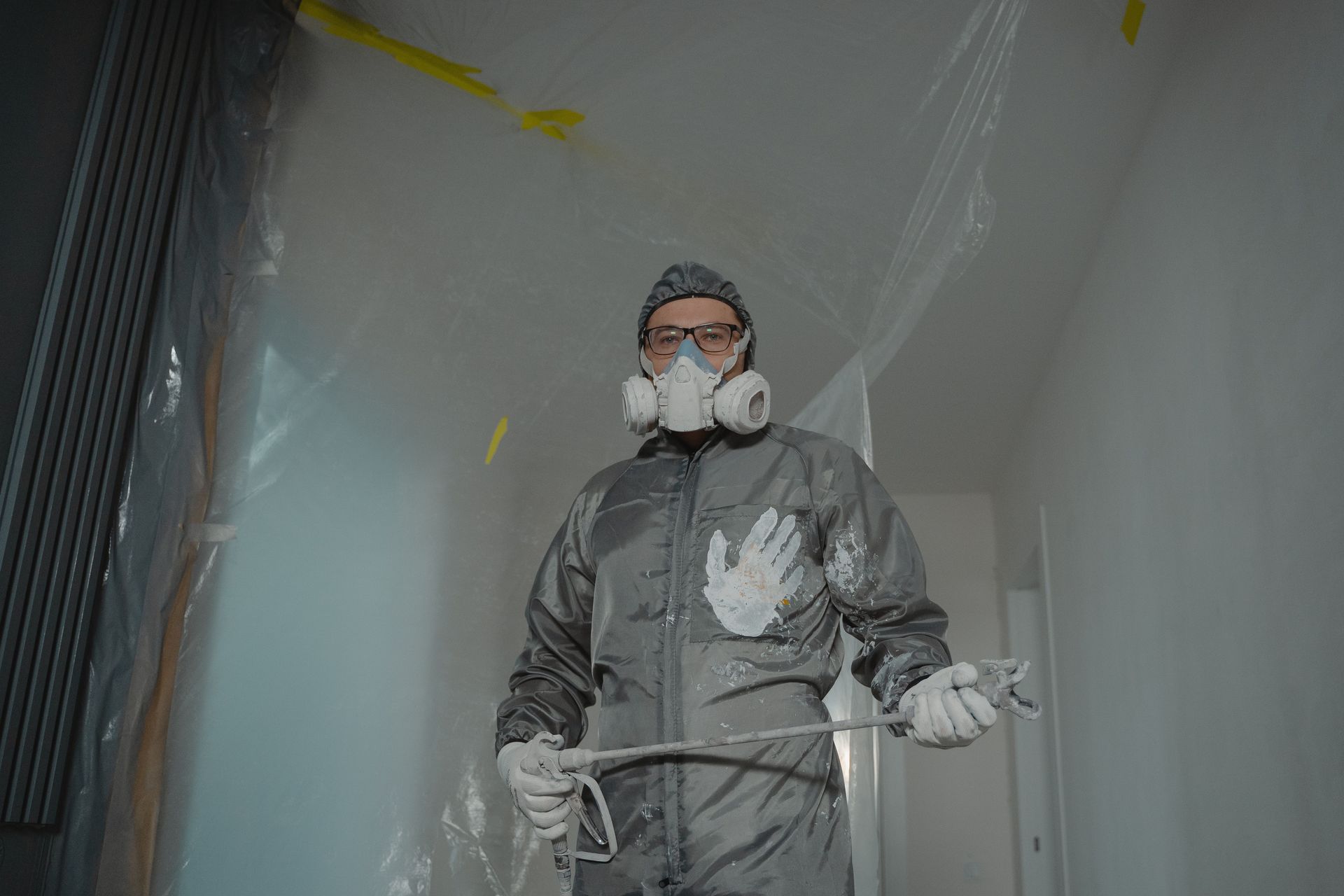 Worker in protective suit and respirator painting a wall indoors.