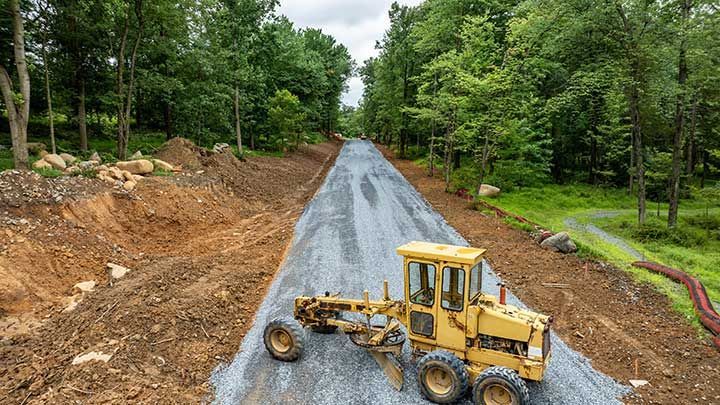 Heavy machinery is grading a recently constructed gravel road 