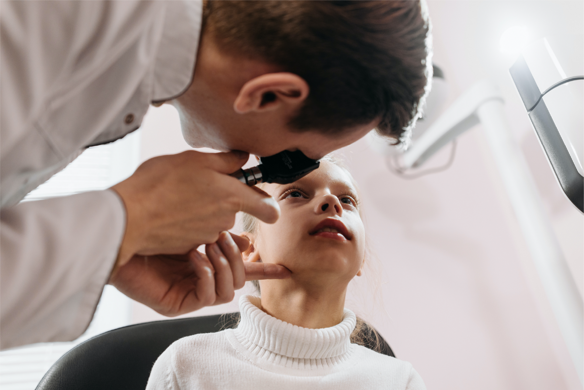 Doctor examines a child's eye with an otoscope in a clinical setting; doctor points to child's face.