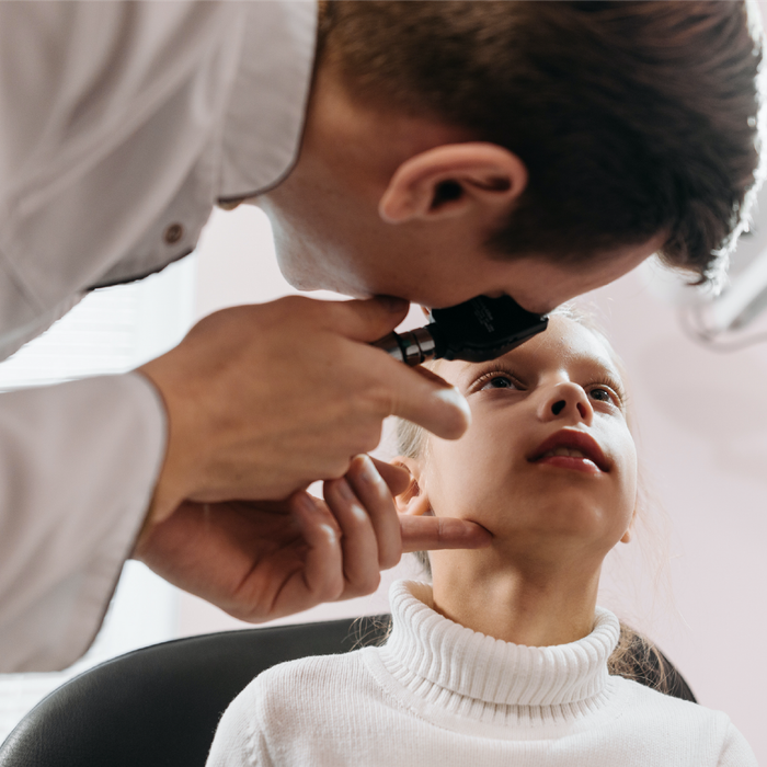 Doctor examining a child's ear with an otoscope. The child is looking up. The setting is likely a medical office.