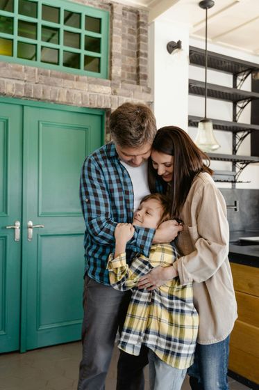 Family hugging in a home entryway beside a green door and stairs.