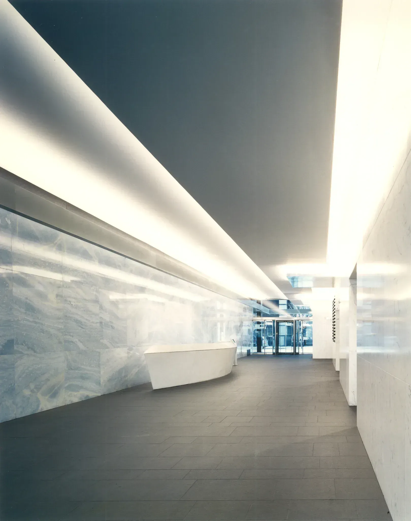 Interior view of a long, modern hallway with white walls and a dark floor.