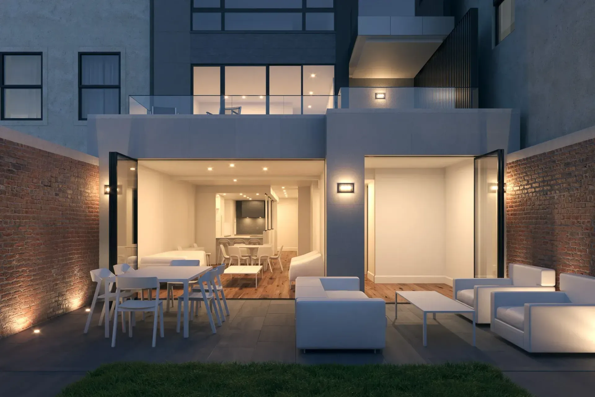 Backyard patio with lit walls, white furniture, and an open kitchen at night.