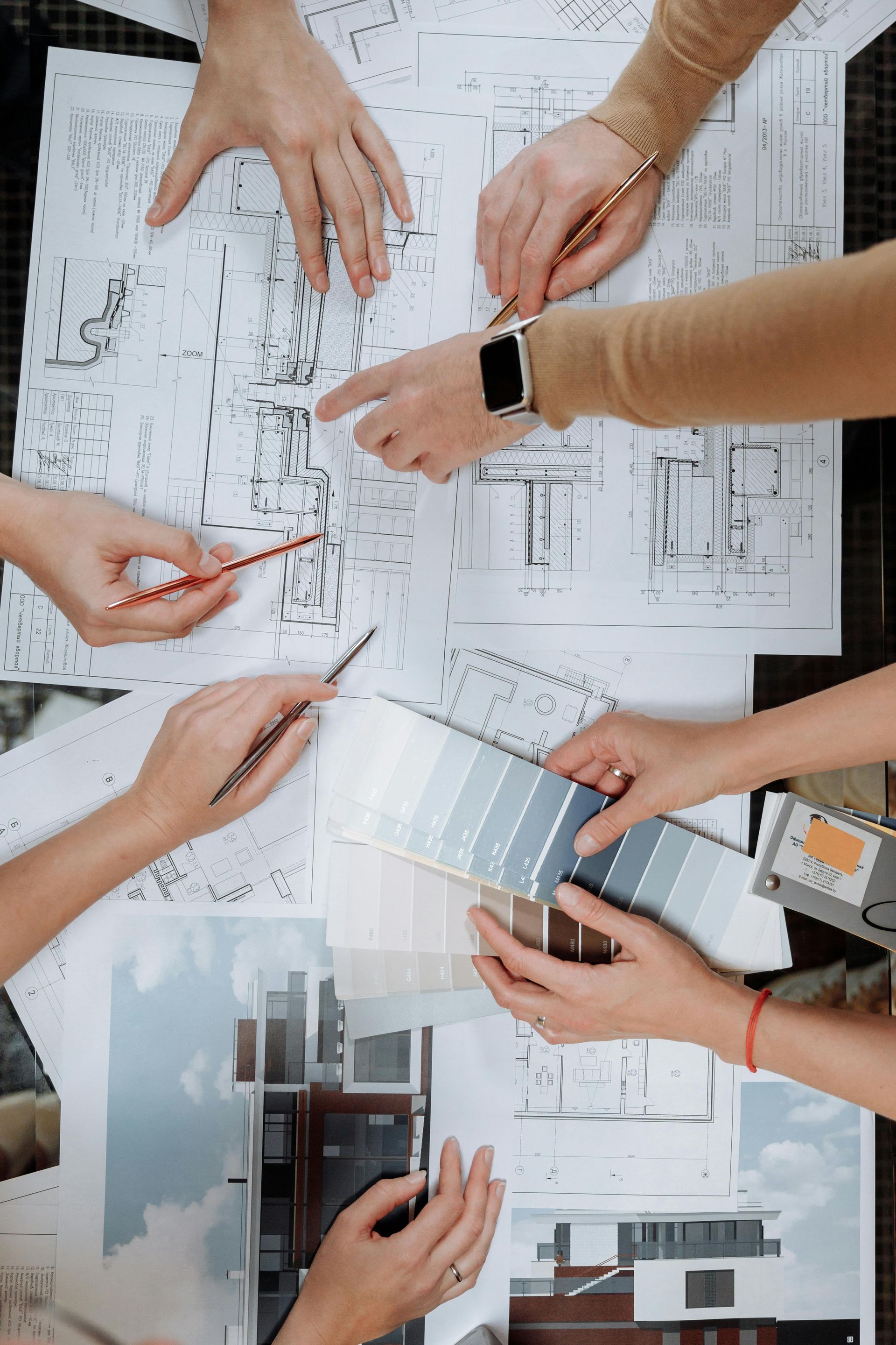 Hands examining blueprints, color swatches, and architectural photos on a table.