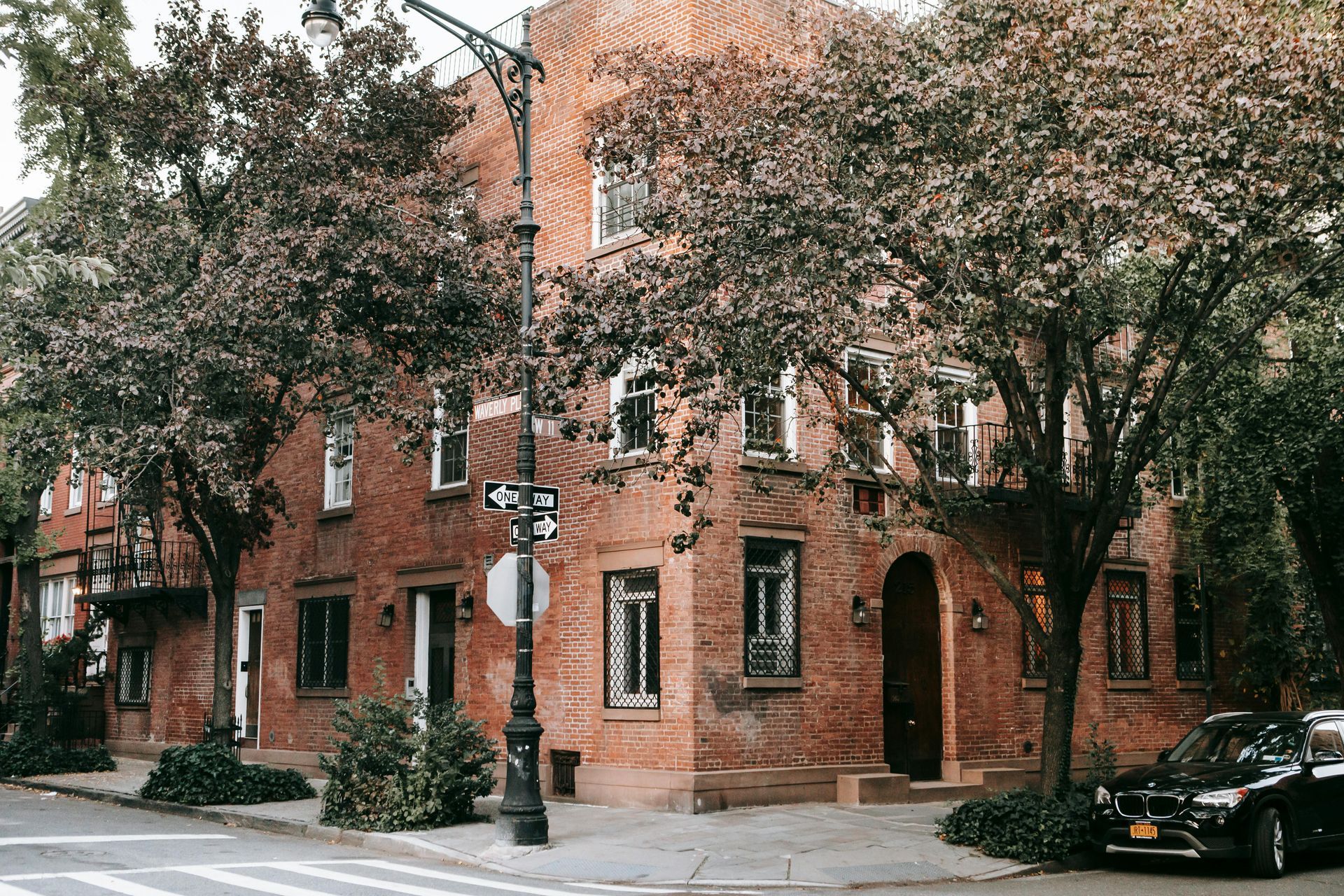 Brick building on a corner with trees, a street sign, and a black car.