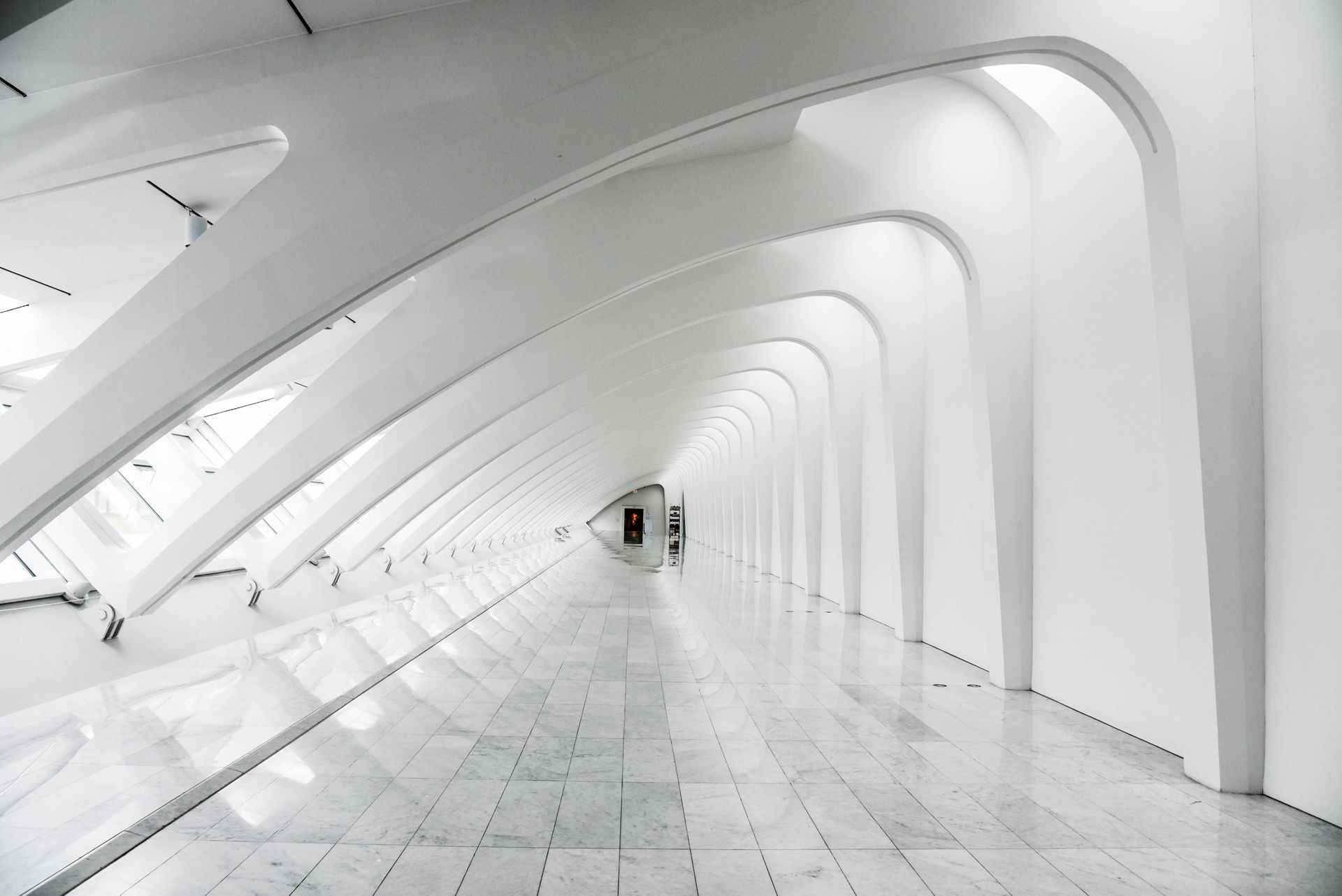 White, arched hallway in modern building with tiled floor and bright lighting.