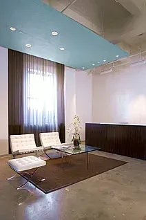 Modern office reception area with white chairs, dark wood reception desk, and blue ceiling panel.