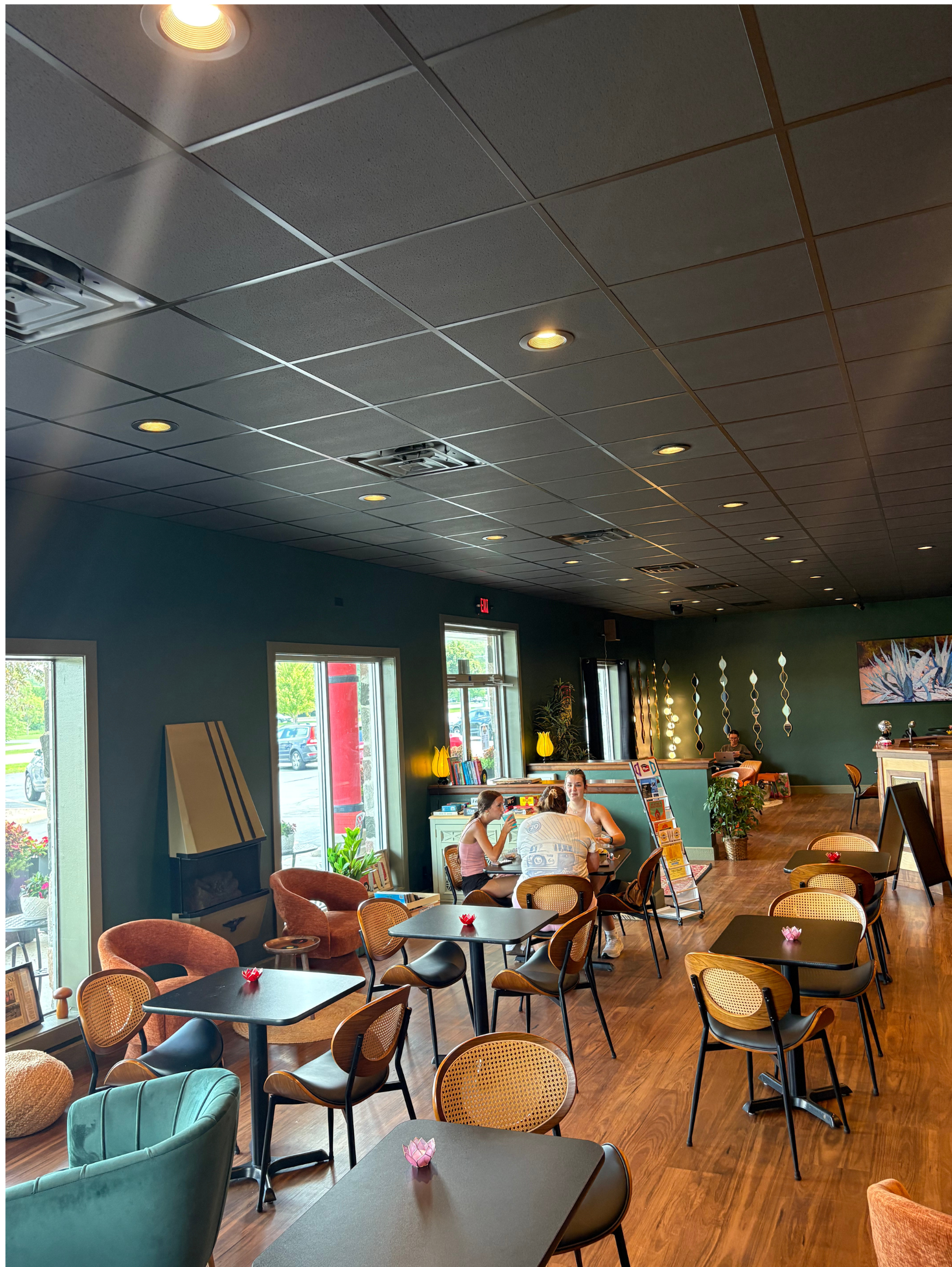 Interior of a cafe with tables, chairs, and seated customers; teal walls and dark ceiling.