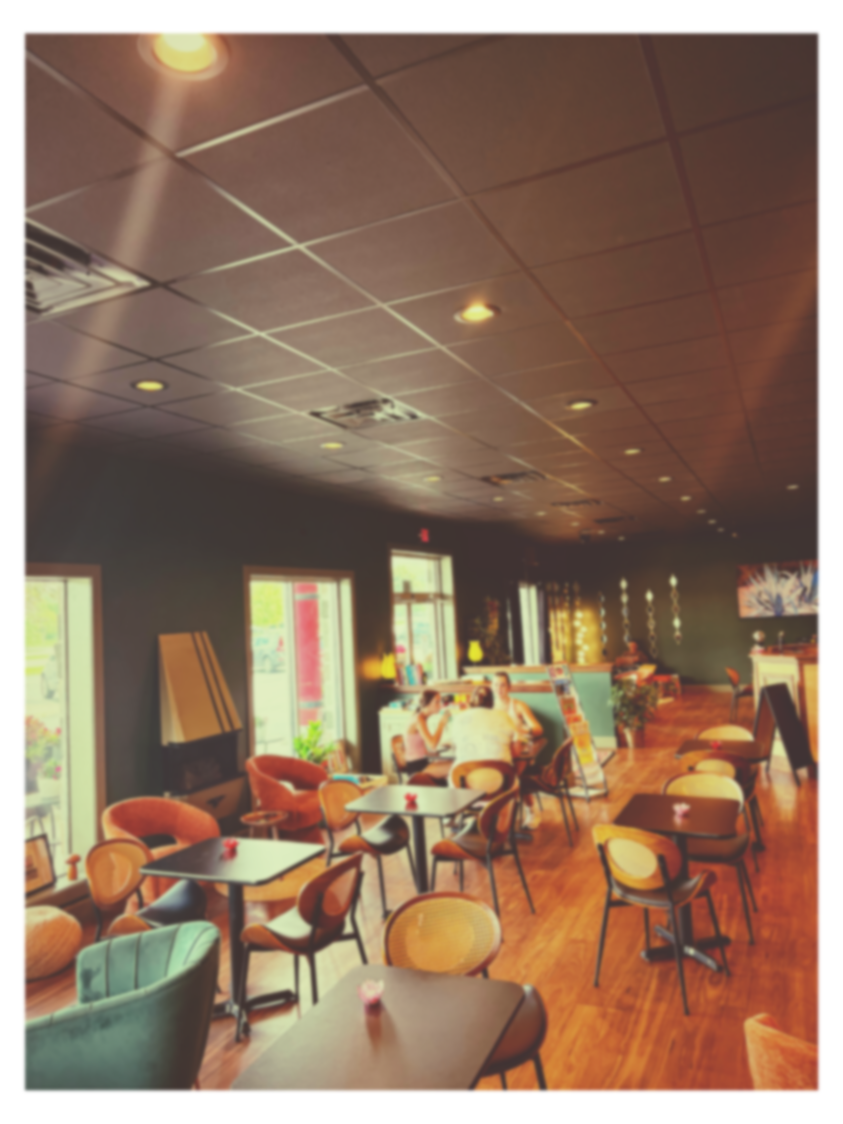Interior of a cafe with tables and chairs, people seated, windows with natural light, and a wooden floor.