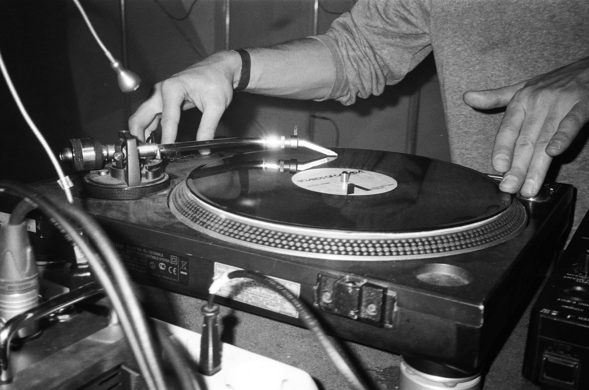 DJ's hands on turntable, adjusting vinyl. Black and white photo in a club setting.