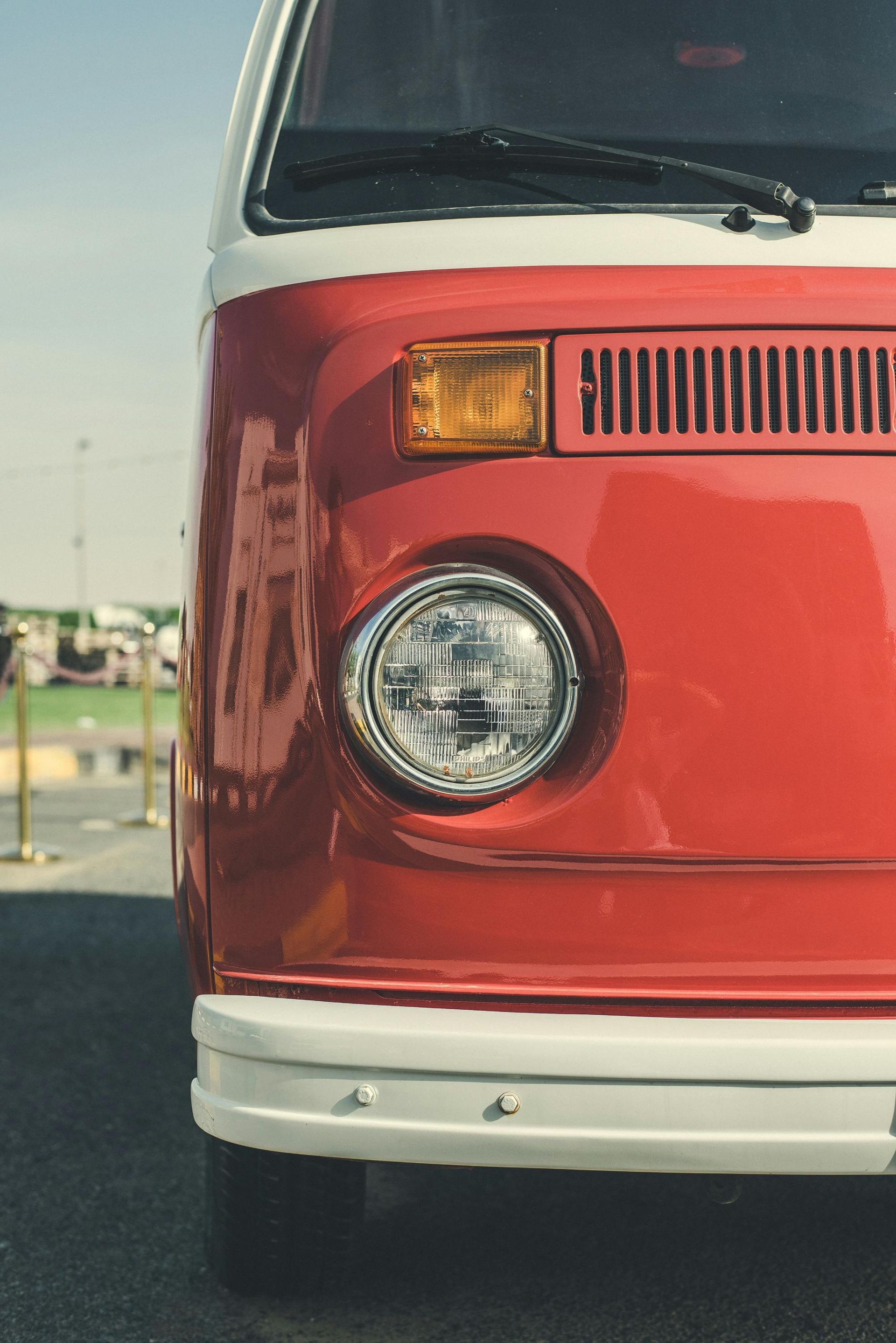 Red and white vintage Volkswagen van front view, with a round headlight.