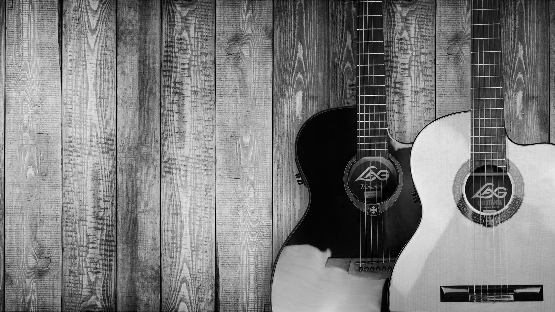 Two acoustic guitars leaning against a weathered wooden wall, in black and white.
