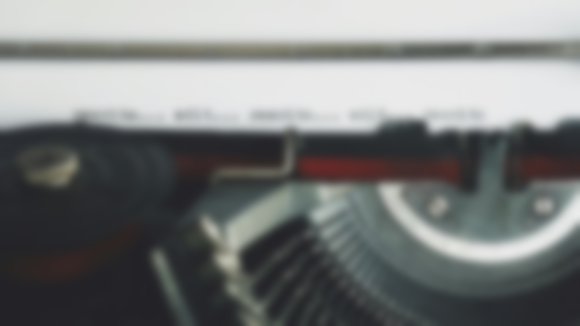 Close-up of a typewriter, red ribbon, partially typed white paper, with a blurred background.