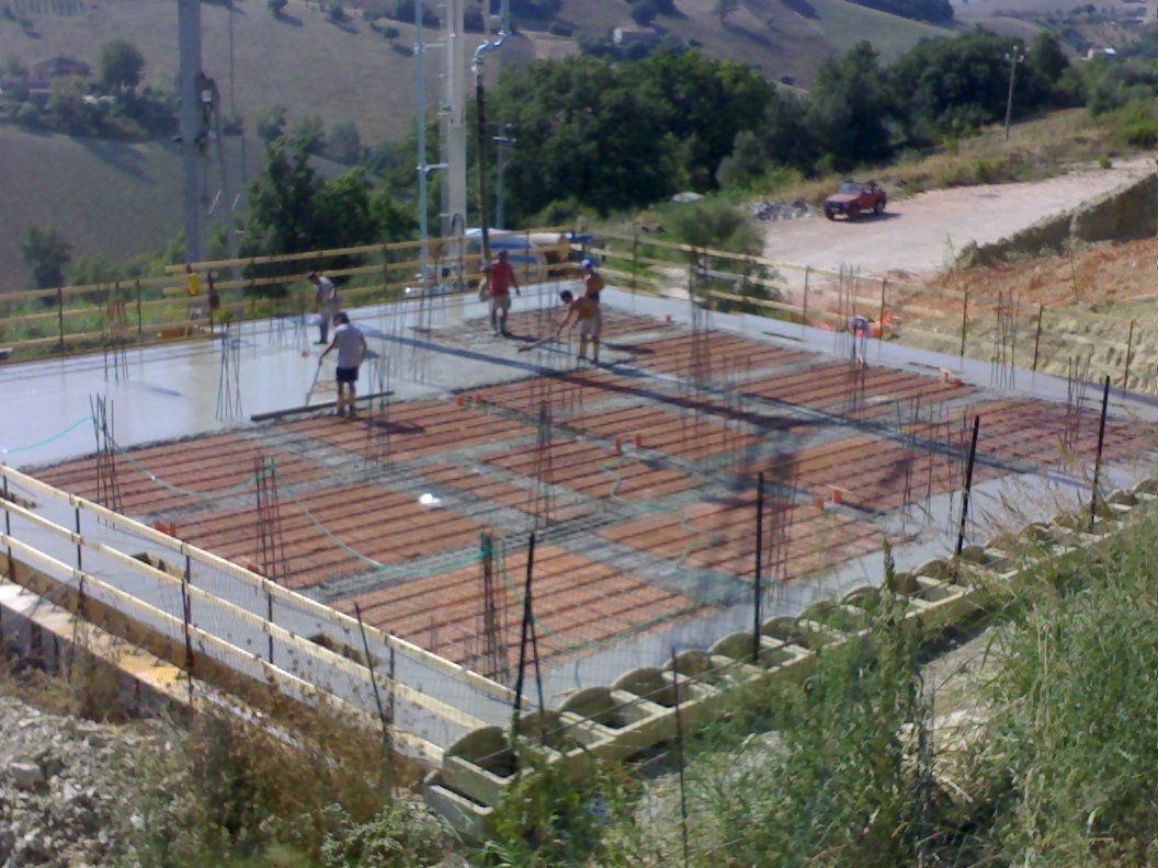 Operai intenti a costruire fondamenta in cemento armato su un cantiere in collina, utilizzando barre d'armatura e impalcature.