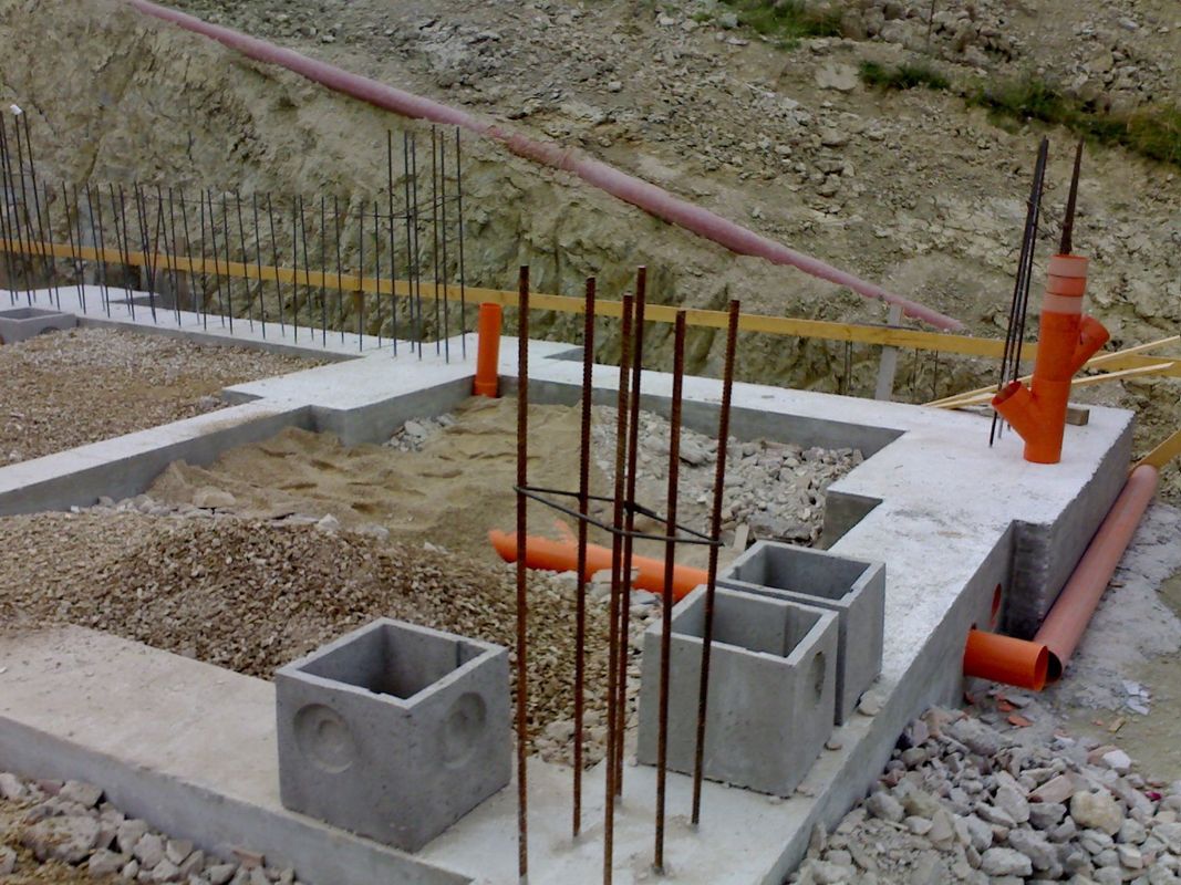 Fondamenta in cemento parzialmente realizzate con barre d'armatura, blocchi di cemento e segnaletica di sicurezza arancione su un pendio.