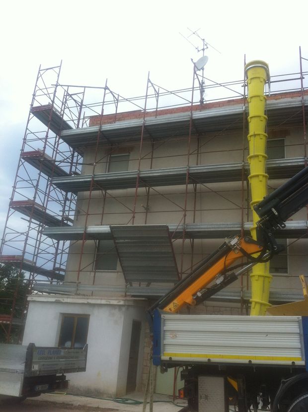 Cantiere edile con impalcature, un edificio in cemento e una piattaforma aerea montata su camion accanto ad esso.
