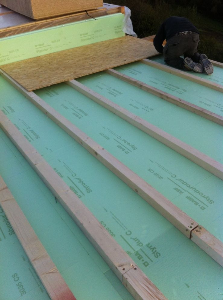 Una persona sta installando pannelli isolanti in schiuma verde su un tetto in costruzione.